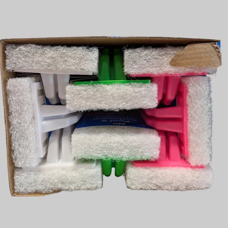 A cardboard box containing several folded white and colored plastic cleaning sponges or scrubbers wrapped in white foam padding, photographed from above on a white surface with a blurred background.
