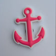 A pink anchor-shaped item with a white outline, photographed on a plain white square card against a light gray surface.